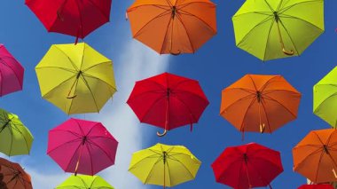 Parlak mavi gökyüzünün altında asılı parlak renkli şemsiyelerin yakın çekimi. Aşağıdan bak. Neşeli şehir kurulumu şenlikli bir atmosfer yaratıyor..
