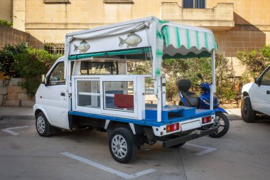 Zabbar, Malta - 06.01.2025: Çizgili tenteli ve balık tabelalı küçük balık teslimat kamyonu, bir Malta kasabasında park edilmiş. Geleneksel deniz ürünleri satıcısı aracı.