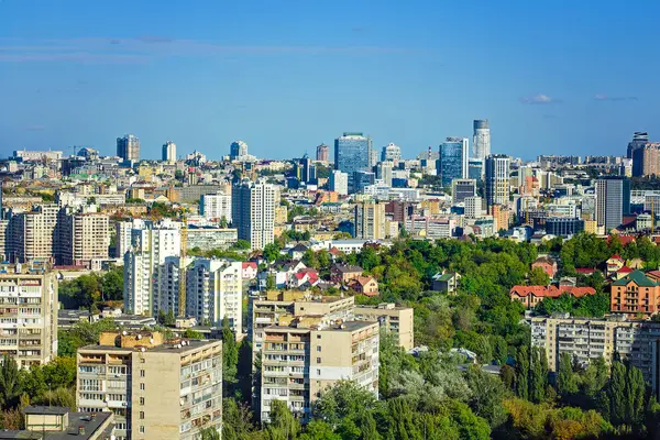Gökdelenlerin ve Sovyet döneminden kalma binaların açık mavi gökyüzü altında yeşil alanlarla çevrili olduğu panoramik bir şehir manzarası..
