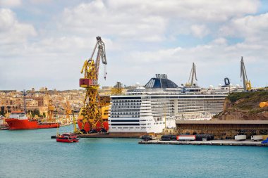 Turkuaz suya ve kıyı kenti siluetine karşı kurulmuş büyük vinçleri, kargo ve yolcu gemileri ve depo altyapısı olan işlek bir Akdeniz sanayi limanı..