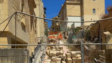 Kireç taşı blokları, metal çitleri ve güneşli bir günde dar bir sokağı kapatan ahşap tahtalarla dolu dağınık kentsel inşaat alanı..