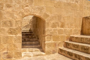 Güneşli bir günde sıcak dokusu, kemeri ve eski merdivenleri olan tarihi bir kale duvarının yakın çekimi. Adımların ve gölgelerin geometrik çizgileri görsel bir ritim yaratır..