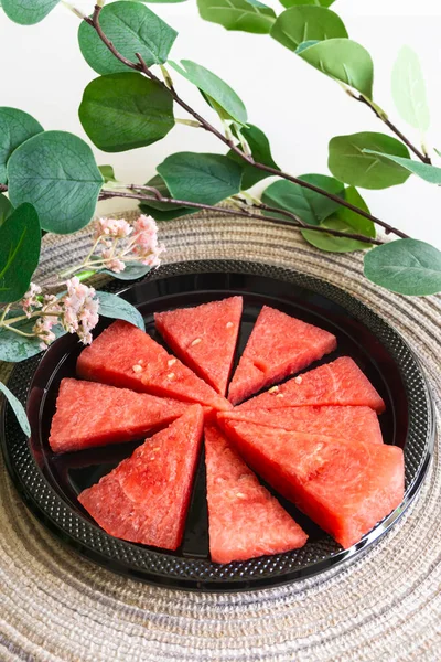 Serving size sliced watermelon on a black plate with some leaves and flowers. Vertical shot.