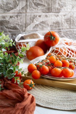 Sürdürülebilir alışveriş poşetinde kırmızı domatesler ve ahşap tepside yeşil yapraklı kiraz domatesleri..