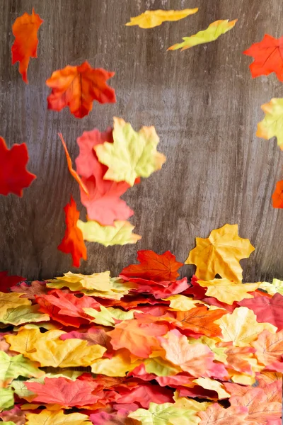Colorful autumn leaves falling over fall leaves. Wooden background. Studio shot. Vertical shot
