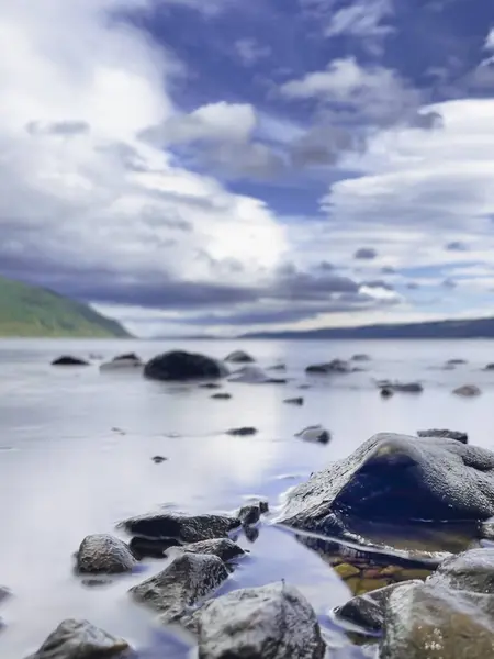 尼斯湖和多云的蓝天 有选择地把重点放在前景中的岩石上 带有复制空间的垂直射击 — 图库照片