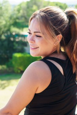 At kuyruklu İspanyol genç bir kadının yan görünüşü. Gülümsüyor ve doğa ile bakışlarını kaçırıyor. Dikey.