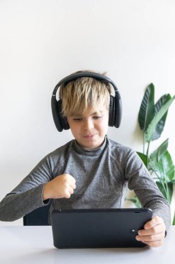 Sarışın İspanyol çocuk dijital tablet ve kulaklıkla oynarken kazanan olarak el kol hareketi yapıyor..