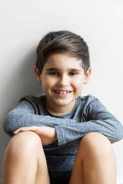 İspanyol çocuk, 8 yaşında, mutlu bir ifadeyle gülümsüyor, dizleri bükük oturuyor..