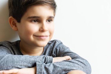 Kollarını kavuşturmuş, duvara yaslanmış gülümseyen tatlı bir çocuk. Kopya alanı ile yatay çekim.