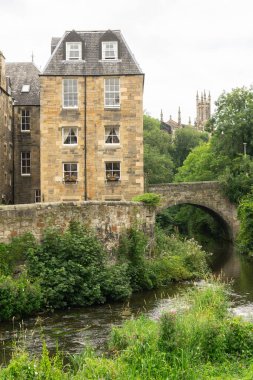 Geleneksel taş binalar ve yemyeşil yeşilliklerin yer aldığı İskoçya 'nın Edinburgh kentindeki Leith Suyu üzerindeki eski taş köprüsü ile tarihi Dean Village manzarası.