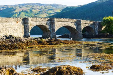 Tarihi Eilean Donan Kalesi köprüsünün manzarası, İngiltere, İskoçya 'da günbatımında sakin suları yansıtıyor.