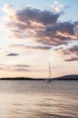 Gün batımında İskoçya 'da güzel pembe ve mor bulutlarla dolu sakin bir denize demirlemiş yelkenli.