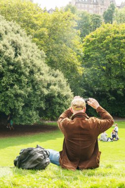 Edinburg, İskoçya - 20 Ağustos 2023: Princes Street Gardens 'ta arka planda Edinburgh Kalesi ile çimlerin üzerinde oturan adam