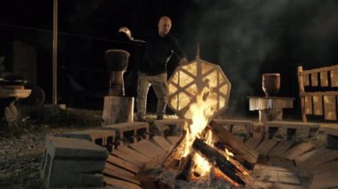 Bir adam djembe ve çerçeve davulu gibi etnik davul çalıyor, meditasyon ve gece ateşin yanında ayinler için mistik bir ortam yaratıyor. 4k görüntü