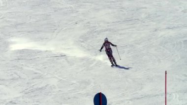 Şık bir kayak kıyafeti giymiş bir bayan sporcu hızla yamaçtan inip, oyma dönüşünü gerçekleştirir. Gerçek zamanlı görüntüler, profesyonel kayak tekniğinin hızını, hassasiyetini ve tekniğini yakalar..