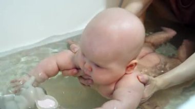 Bir bebek sıcak banyo suyunda yüzmeyi evde öğrenir. Bir ebeveyn bebeğe destek olur, çocuk oyuncağa uzanır ve ilk su hareketlerini uygular..