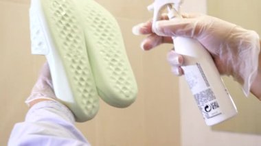 Koruyucu eldiven giyen bir işçi tabanlara antiseptik sıkarak terlikleri dezenfekte eder. İşlem, bir kaplıca, sauna ya da hamam gibi fayanslı bir ortamda gerçekleşiyor..