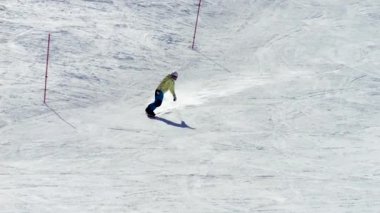 Sarı ceketli ve koruyucu miğferli bir sporcu kar kayağına ustalıkla kayıyor. 4K yavaş çekim, yumuşak hareket, hız ve snowboard tekniğini vurguluyor..