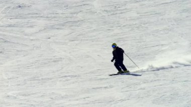 Kış kıyafetleri içinde bir sporcu ve bir kask yavaşça karlı yamaçtan aşağı kayarak kontrolü sağlıyor. Yavaş çekim 4K kayaklardaki her hareketi ve dengeyi yakalar..