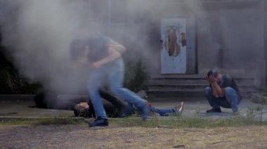 Acımasız bir sokak kavgasından sonra iki yaralı hemen ayrıldı. Biri acı içinde yüzünü tutuyor, diğeri aceleyle uzaklaşıyor. Kurbanlar yerde yatarken duman etrafa yayılıyor ve kaotik bir atmosfer yaratıyor..