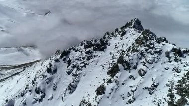 Kazakistan 'daki Büyük Almaty Tepesi' nin kayalık, karlı sırtı üzerinde insansız hava aracı görüntüsü. Arkaplanda kalın bulutlar ve mavi gökyüzü var. Seyahat, doğa ve sinematik çekim için mükemmel..