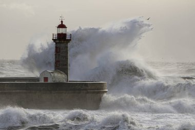 Huge wave splash over old lighthouse at sunset.