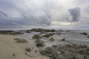 Bulutlu yaz mevsiminde alacakaranlıkta ya da gün batımında deniz manzarası. Kuzey Portekiz kayalık kıyısı kumsalda yosun görüyor..