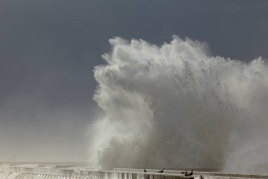 Büyük fırtınalı deniz dalgaları İskeleye sıçrıyor ve püskürtüyor.