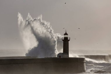 Yumuşak arka ışıklandırmalı fırtınalı deniz dalgası sıçraması. Douro nehri ağzı eski iskele ve deniz feneri, Porto, Portekiz. Kış gece yarısı ışığı.