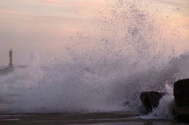 Gün batımında dalgalı deniz. Nehir ağzı iskelesi ve fener, Vila do Conde, Portekiz 'in kuzeyi.