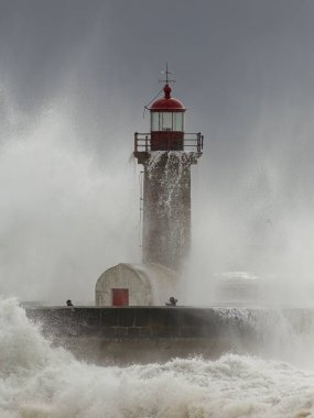 Porto, Portugal - February 7, 2016: Douro river mouth old lighthouse during storm seeing people running away from the splash of sea waves.