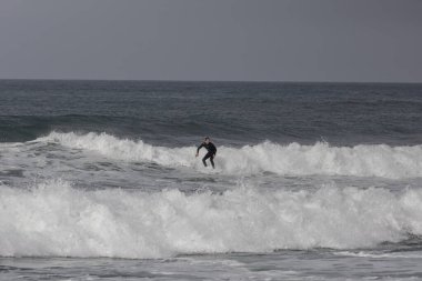 Praia do Cabo do Mundo, Portekiz - 30 Ekim 2024: Portekiz 'in kuzey kıyılarında beyaz dalgalarda sörfçü 