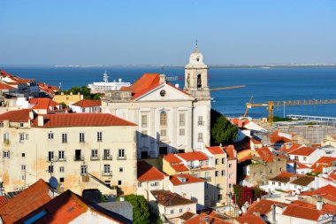 Lizbon, Portekiz 'in Alfama ilçesinin panoramik manzarası, önde Igreja de Santo Estvo (St. Stephen Kilisesi) ve arkada Tagus Nehri yer almaktadır.