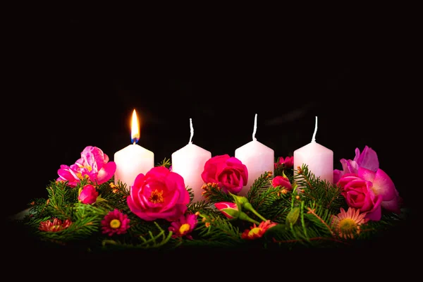 first burning advent candle on decorated rose flower pink advent wreath