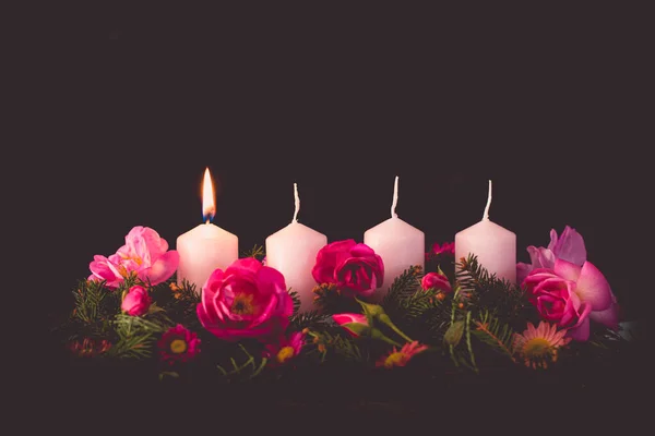 first burning advent candle on decorated rose flower pink advent wreath