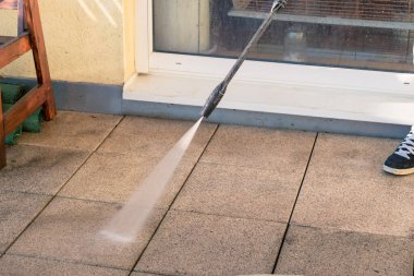 man with tube cleaning terrace with water pressure from dirt