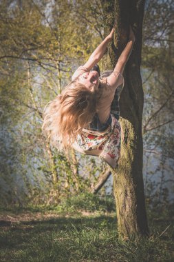 happy girl climbing up the tree in vivid green spring nature