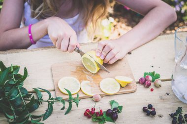 Bıçaklı el, limon dilimleri, masada nane ve böğürtlen meyveleri