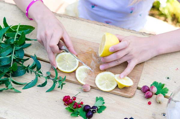 Bıçaklı el, limon dilimleri, masada nane ve böğürtlen meyveleri