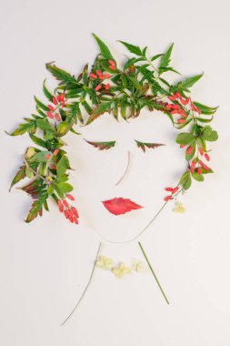 Beyaz arka planda izole edilmiş yeşil sonbahar yaprakları ve çiçeklerinden yapılmış kadın yüzü