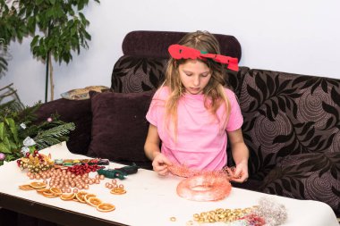 Güzel kız Noel çelengi yapıyor. Mücevherlerle süslenmiş ve diğer renkli süslemelerle süslenmiş.