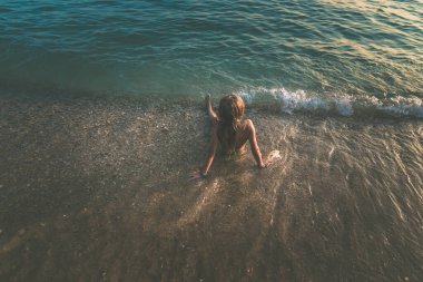 Deniz kenarında kumların üzerinde oturan tatlı bir genç kız., 