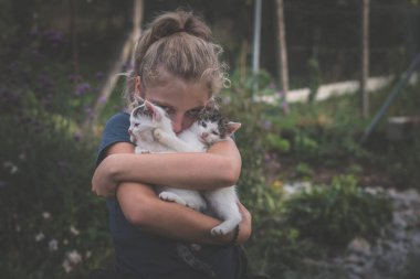 Sarışın kız bahçede iki kedi tutuyor.