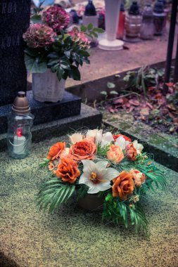 Fenerlerle süslenmiş mezarlar, yanan mumlar, renkli kasımpatı çiçekleri, katolik semboller.