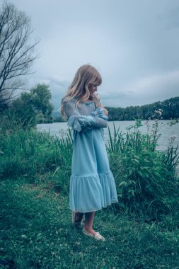 Kırsaldaki nehrin kıyısında yeşil çayırlarda mavi elbiseli güzel bir kız.