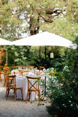 Arka bahçe düğün resepsiyonu - beyaz masa örtülü yuvarlak masalar, klasik fenerler, güller ve sümbül sandalyeler,