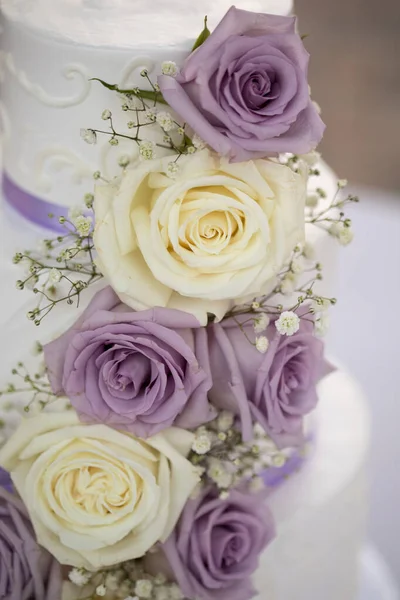 Three tiered wedding cake with lilac and cream roses and purple ribbon