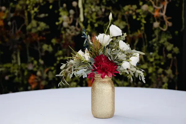 stock image Outdoor wedding reception - guest table decor. Golden glitter vase with burgundy peonies, eucalyptus leaves floral arrangement