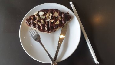 Parlak bir çatalla mükemmel tamamlanmış el değmemiş beyaz bir tabakta bozulmuş bir dilim çikolatalı pastanın tadını çıkar.